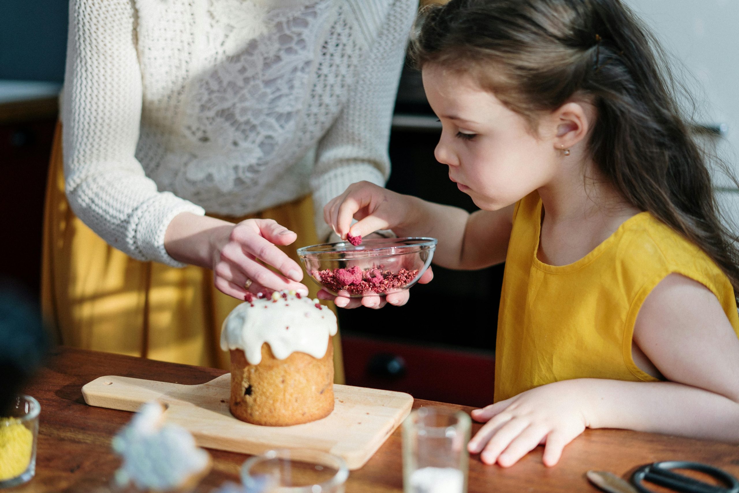 A mother and daughter bonding while decorating an Easter cake together indoors.